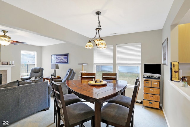 dining space with visible vents, ceiling fan with notable chandelier, a fireplace, baseboards, and light colored carpet