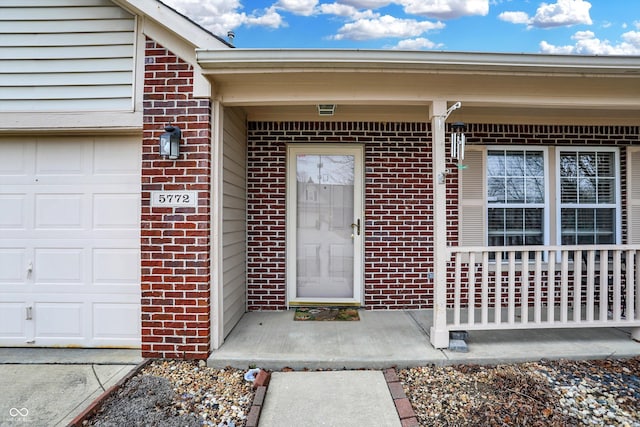 view of exterior entry with a porch and brick siding