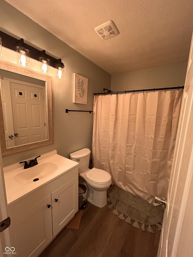 full bathroom with visible vents, toilet, vanity, wood finished floors, and a textured ceiling