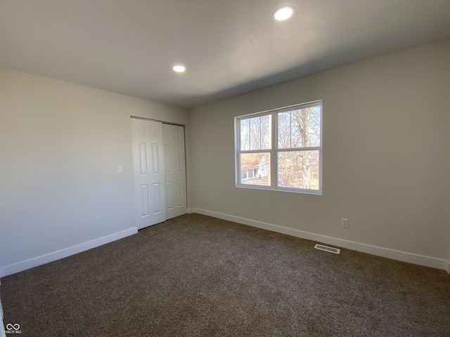 unfurnished bedroom featuring visible vents, recessed lighting, a closet, dark colored carpet, and baseboards