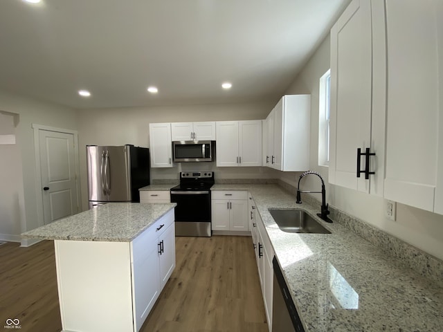 kitchen featuring light stone counters, light wood-style flooring, a sink, appliances with stainless steel finishes, and white cabinetry