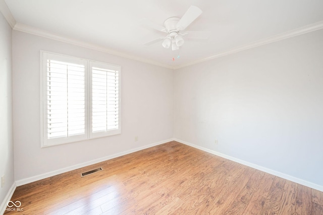 empty room with crown molding, wood finished floors, visible vents, and baseboards