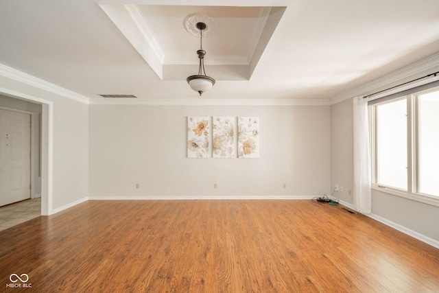 spare room featuring visible vents, baseboards, crown molding, light wood finished floors, and a raised ceiling