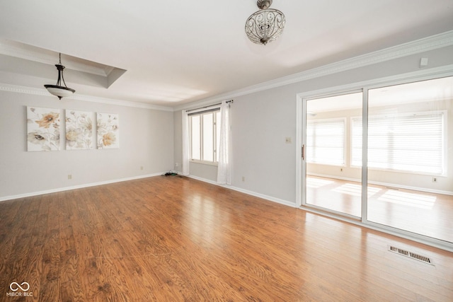 empty room featuring visible vents, wood finished floors, baseboards, and ornamental molding