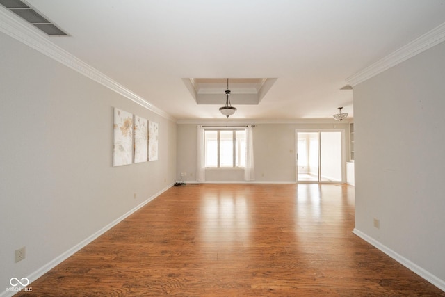 empty room featuring visible vents, wood finished floors, baseboards, crown molding, and a raised ceiling