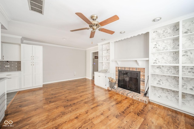 unfurnished living room featuring visible vents, ornamental molding, a ceiling fan, wood finished floors, and a brick fireplace