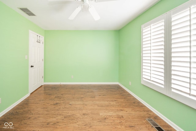 spare room with a ceiling fan, wood finished floors, visible vents, and baseboards