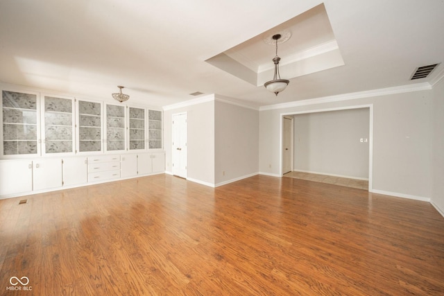 empty room with visible vents, a chandelier, a tray ceiling, ornamental molding, and wood finished floors