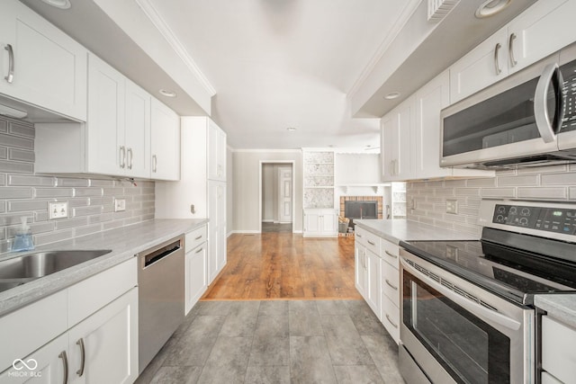 kitchen with light wood-type flooring, appliances with stainless steel finishes, white cabinets, crown molding, and decorative backsplash