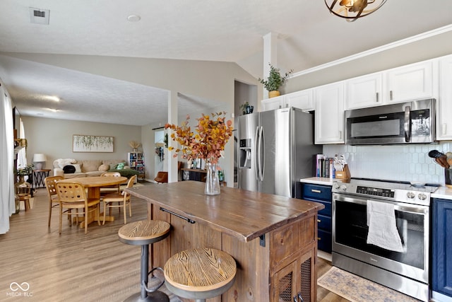 12612 Clearview Ln, Indianapolis, IN 46236 - kitchen featuring appliances with stainless steel finishes, blue cabinets, lofted ceiling, light wood-style flooring, and decorative backsplash