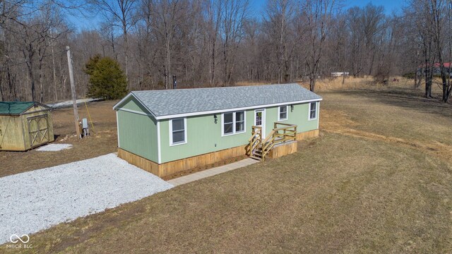 manufactured / mobile home featuring a front yard, a wooded view, driveway, a shingled roof, and an outdoor structure