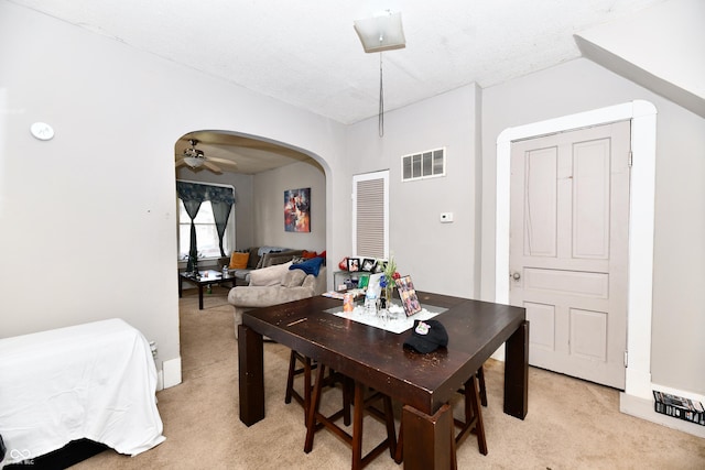 dining room featuring a ceiling fan, visible vents, arched walkways, and light carpet