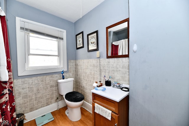 full bath featuring toilet, vanity, wainscoting, wood finished floors, and tile walls