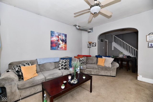 carpeted living area featuring stairway, arched walkways, and ceiling fan