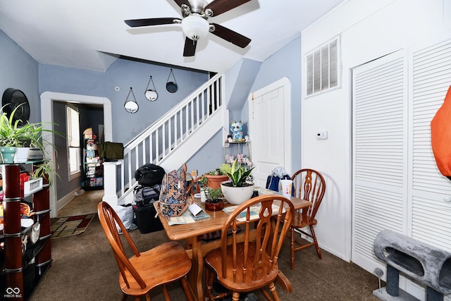 dining room featuring visible vents, dark carpet, ceiling fan, and stairs