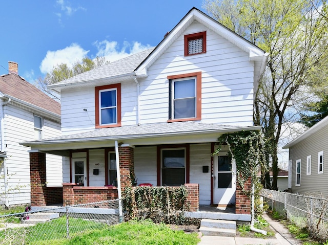 view of front of house featuring brick siding, a porch, a fenced front yard, and roof with shingles