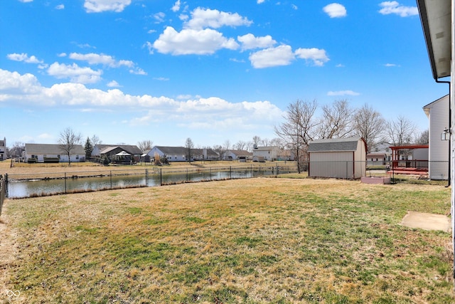 view of yard featuring an outbuilding, fence, a shed, a water view, and a residential view