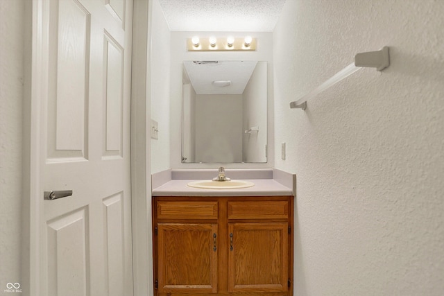 bathroom featuring a textured ceiling, vanity, and a textured wall