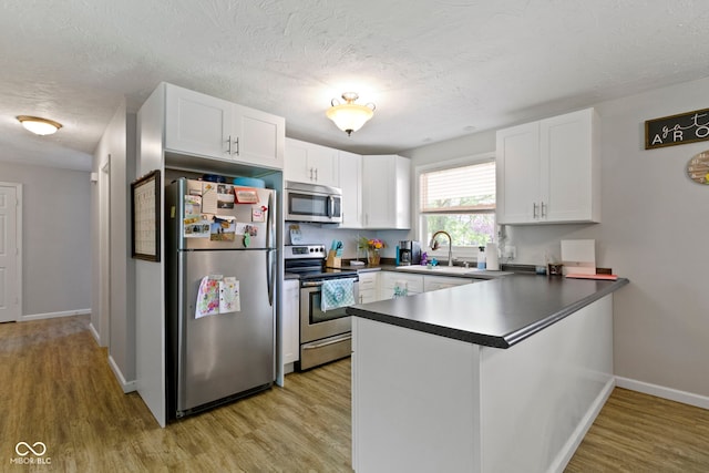 kitchen with a sink, white cabinets, light wood finished floors, a peninsula, and stainless steel appliances