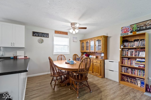 dining space with light wood-type flooring, a textured ceiling, baseboards, and ceiling fan