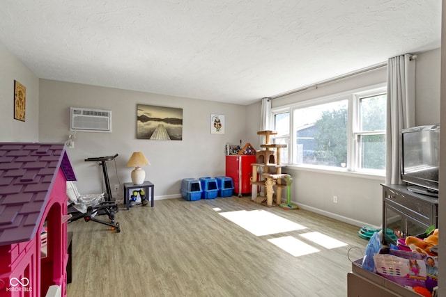 recreation room featuring baseboards, a wall mounted air conditioner, a textured ceiling, and wood finished floors