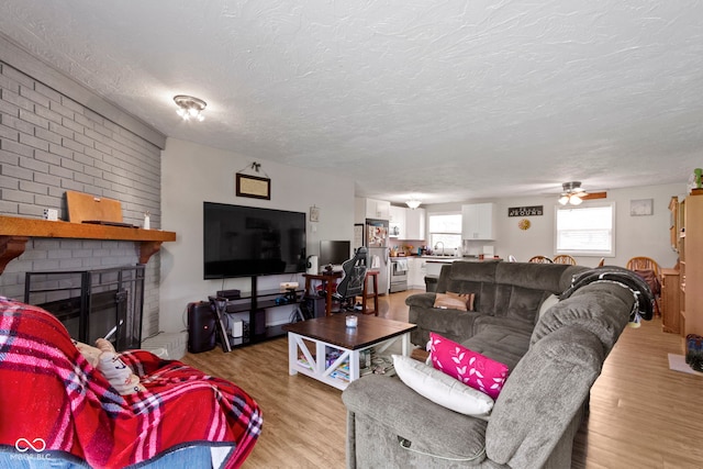 living area featuring a textured ceiling, light wood-style flooring, ceiling fan, and a fireplace