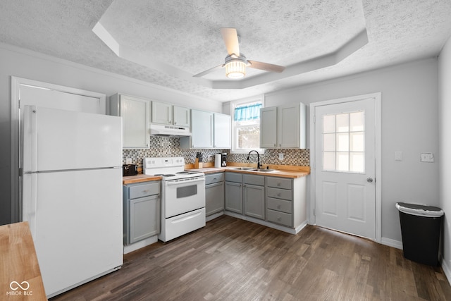 kitchen featuring white appliances, gray cabinetry, a tray ceiling, and under cabinet range hood