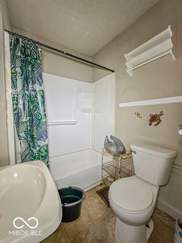 bathroom with tile patterned floors, toilet, shower / bath combo with shower curtain, and a textured ceiling