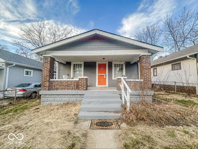 bungalow featuring brick siding, a porch, and fence