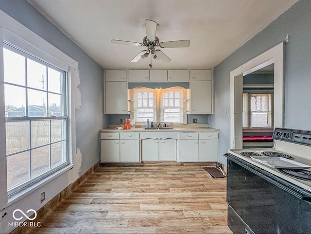 kitchen with light countertops, light wood-style flooring, electric range, white cabinetry, and a sink