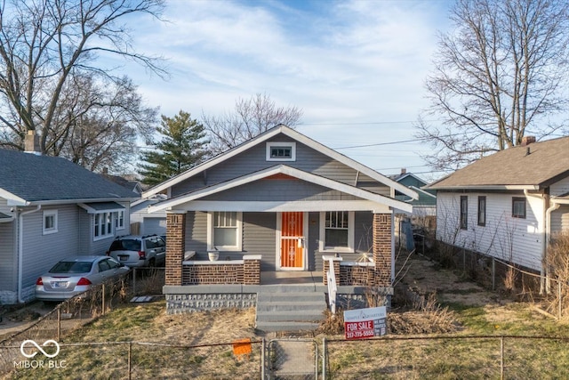 bungalow-style house with a fenced front yard, a porch, brick siding, and a gate