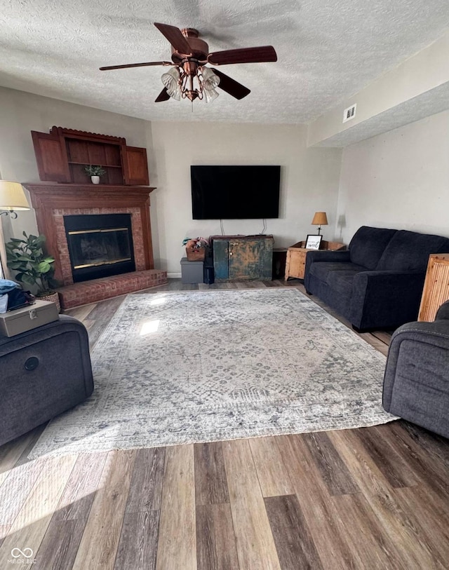 living area with visible vents, a fireplace, a ceiling fan, and wood finished floors