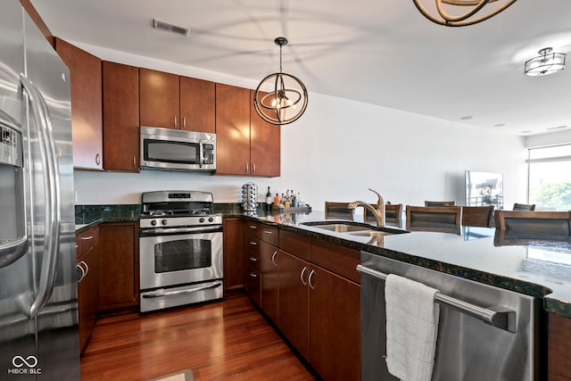 kitchen with visible vents, dark wood finished floors, dark stone countertops, stainless steel appliances, and a sink