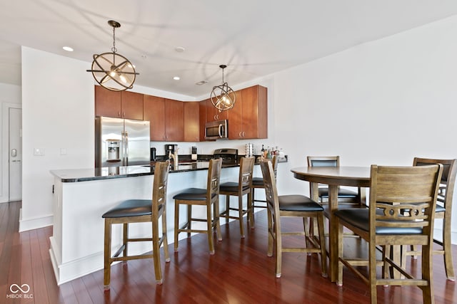 kitchen with decorative light fixtures, a breakfast bar area, appliances with stainless steel finishes, a peninsula, and dark wood-style floors