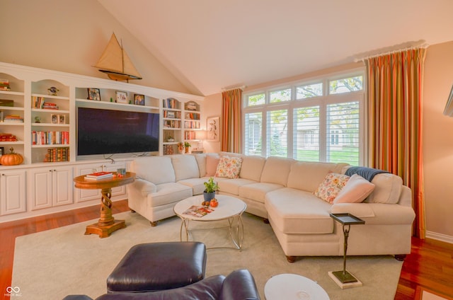 living room with lofted ceiling, built in shelves, and wood finished floors