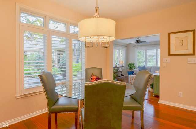 dining space with ceiling fan with notable chandelier, baseboards, and wood finished floors