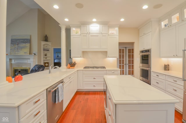 kitchen with a peninsula, light wood finished floors, a kitchen island, appliances with stainless steel finishes, and a sink