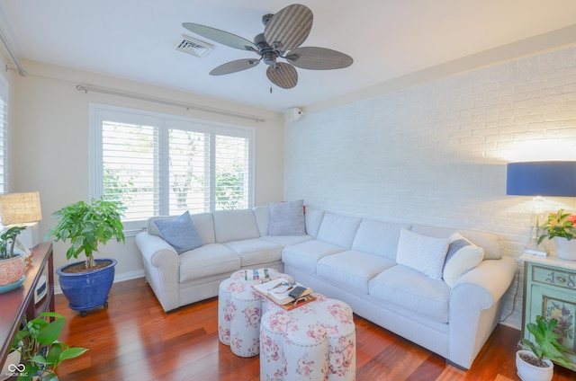 living area with wood finished floors, brick wall, ceiling fan, and visible vents