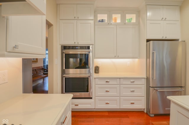 kitchen featuring light countertops, white cabinets, appliances with stainless steel finishes, glass insert cabinets, and wood finished floors