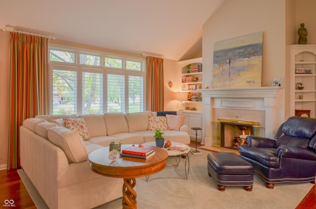 living room featuring built in features, a glass covered fireplace, and vaulted ceiling