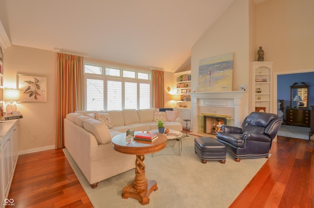living area with built in features, a glass covered fireplace, baseboards, and dark wood finished floors