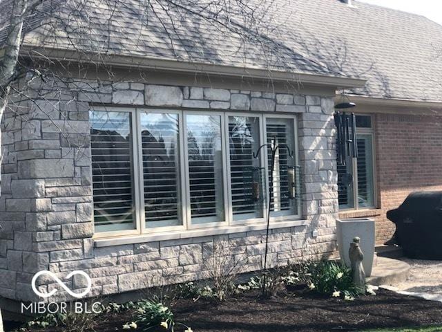 view of property exterior featuring stone siding and roof with shingles