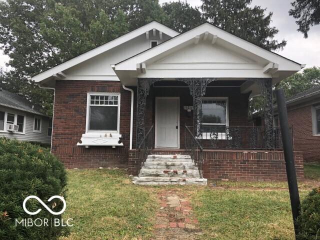 bungalow featuring brick siding, a porch, and a front lawn