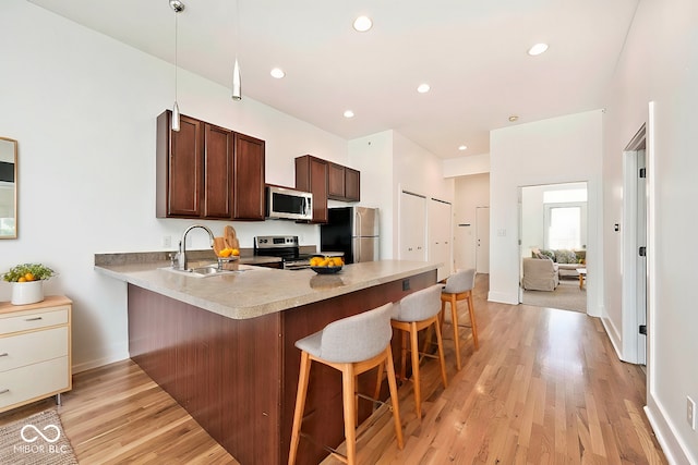 kitchen with a breakfast bar, a peninsula, a sink, light wood-style floors, and appliances with stainless steel finishes