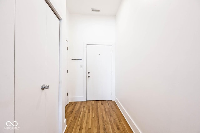 hall with light wood finished floors, visible vents, and baseboards