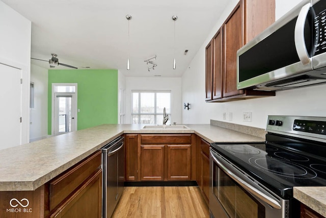 kitchen featuring light countertops, light wood-style flooring, appliances with stainless steel finishes, a peninsula, and a sink