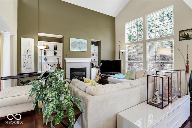 living area with a tiled fireplace, wood finished floors, ornate columns, and high vaulted ceiling