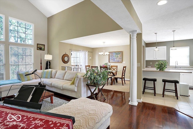 living area with a notable chandelier, high vaulted ceiling, hardwood / wood-style flooring, baseboards, and ornate columns