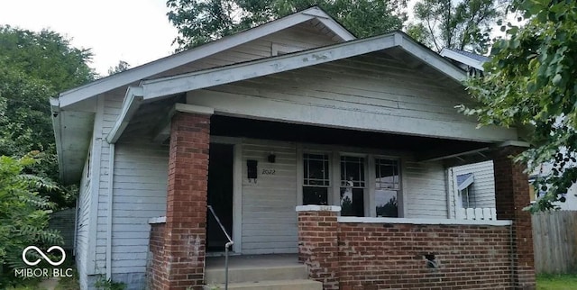 bungalow-style house featuring brick siding, covered porch, and fence