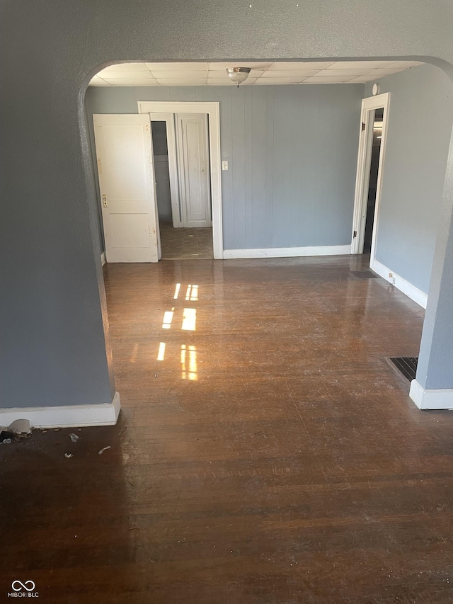 unfurnished room with wood finished floors, arched walkways, and baseboards